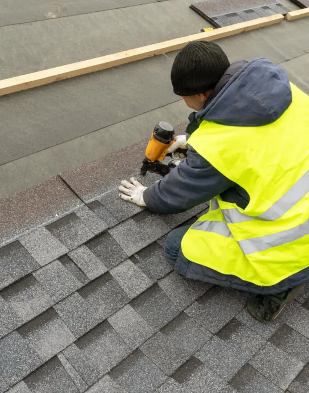 Worker installing asphalt shingles roof with a nail gun.