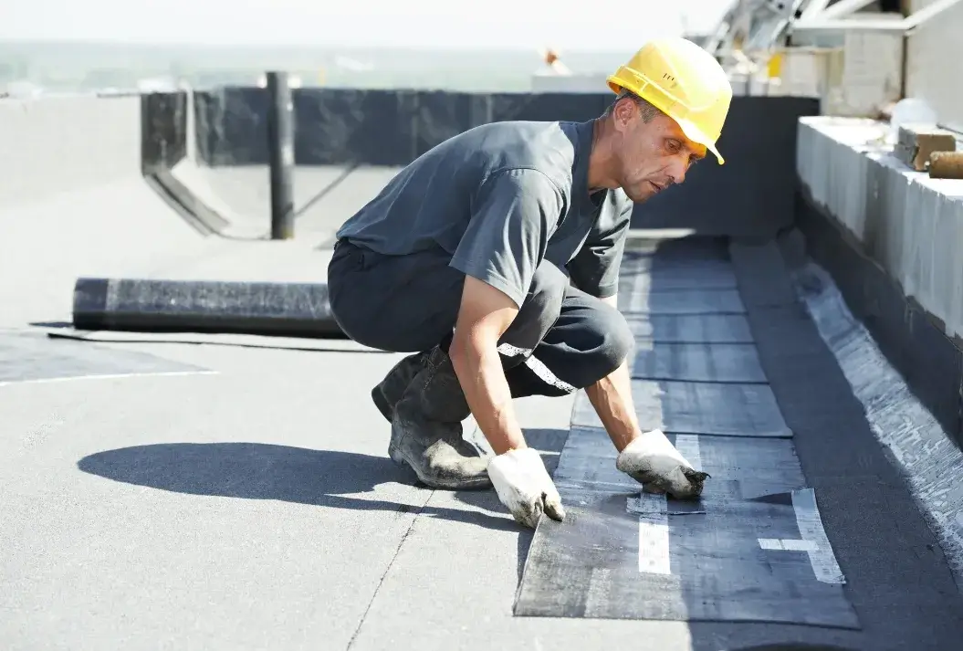 Roofer applying waterproof membrane on a flat commercial roof.