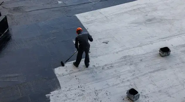 Worker applying waterproofing material to a flat commercial roof.