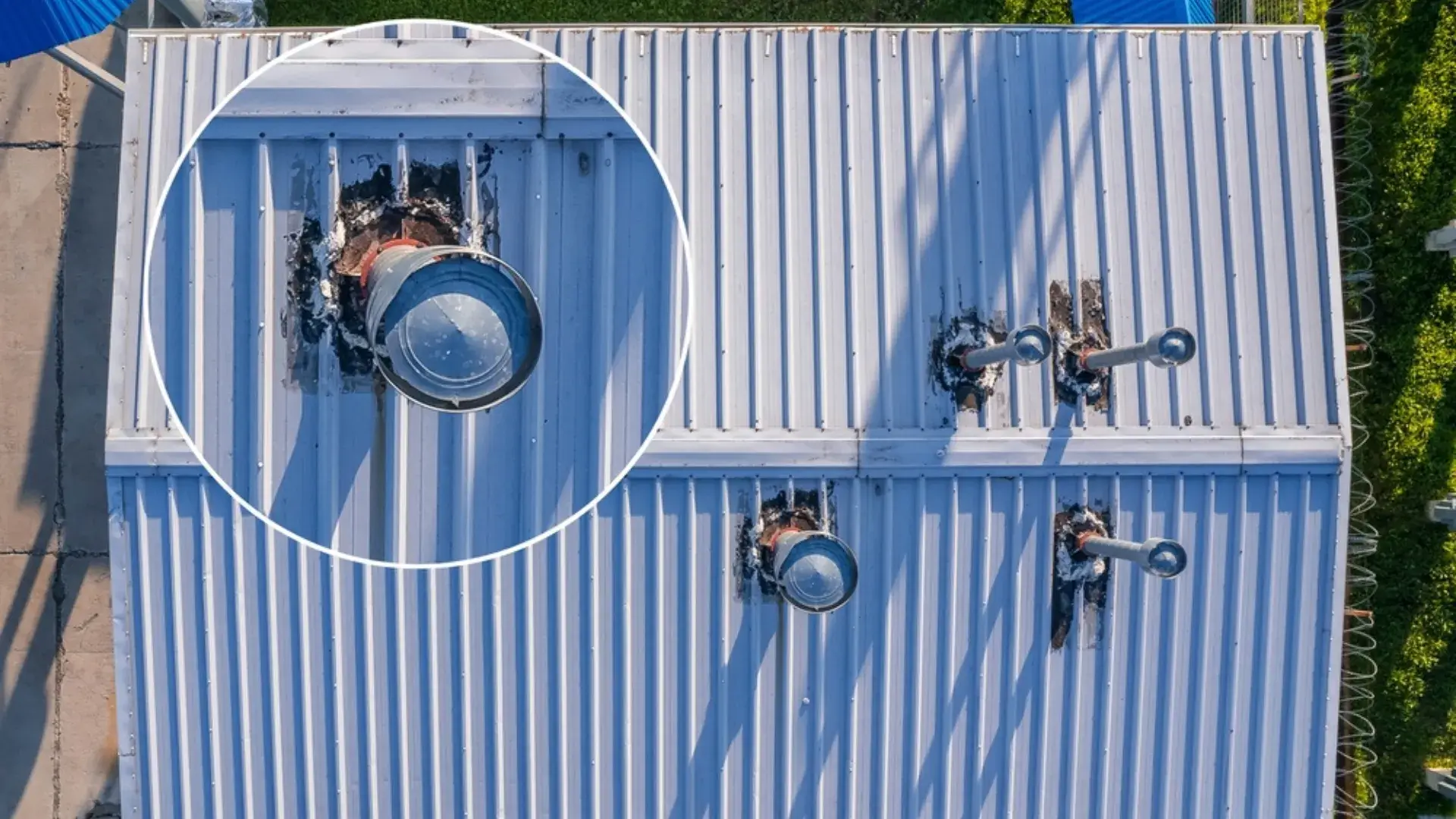 Aerial view of a damaged metal roof with rusted ventilation pipes and deteriorated sealing.