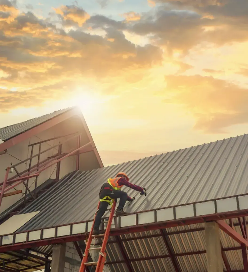 Roofer installing a metal roof on a residential building at sunset.