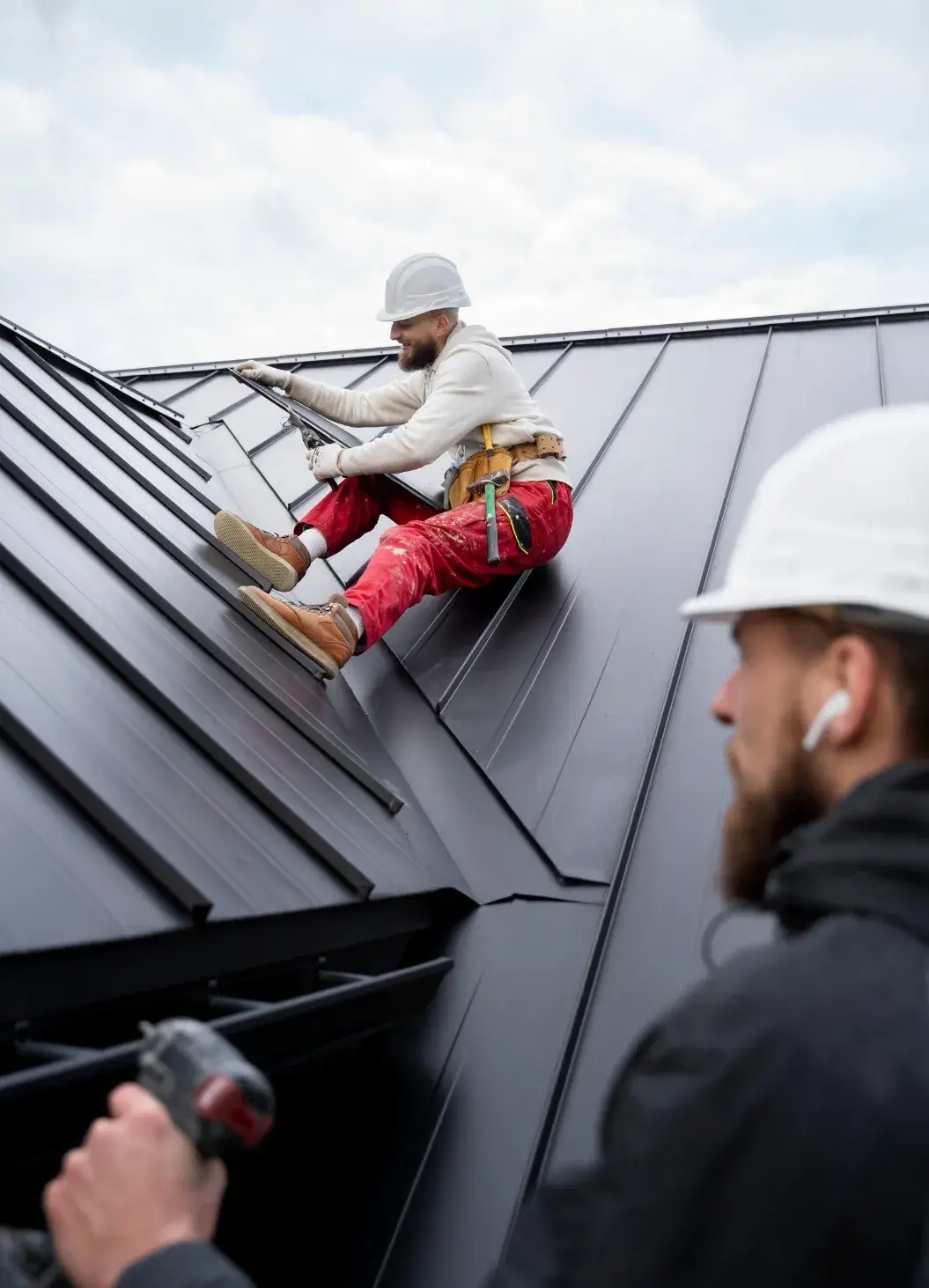 Professional roofers installing a black metal roof while using safety harnesses.