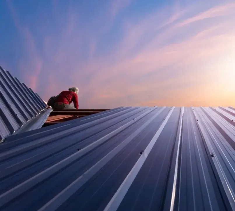 Roofer installing a metal roof at sunset.