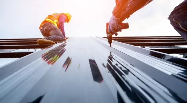 Construction workers installing a metal roof with power drills under sunlight.