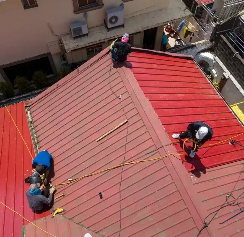 Workers installing a red metal roof on a residential building.