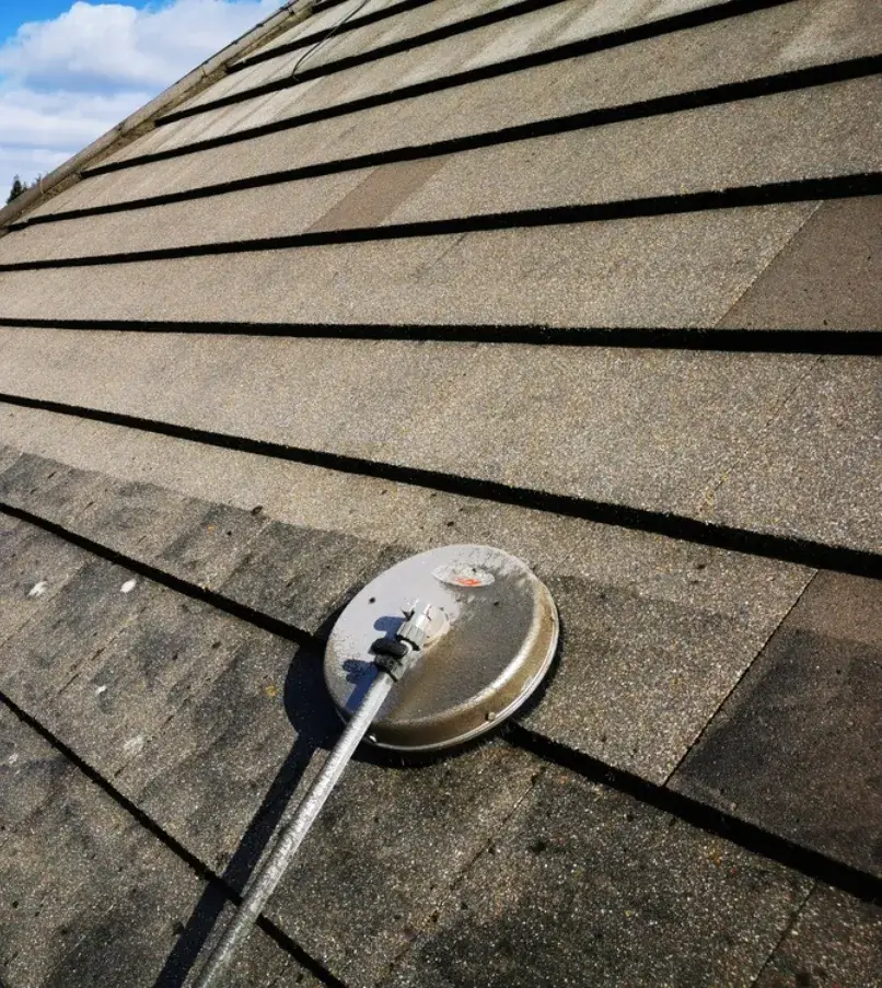 Roof cleaning in progress using a high-pressure washer, showing a contrast between cleaned and dirty shingles.