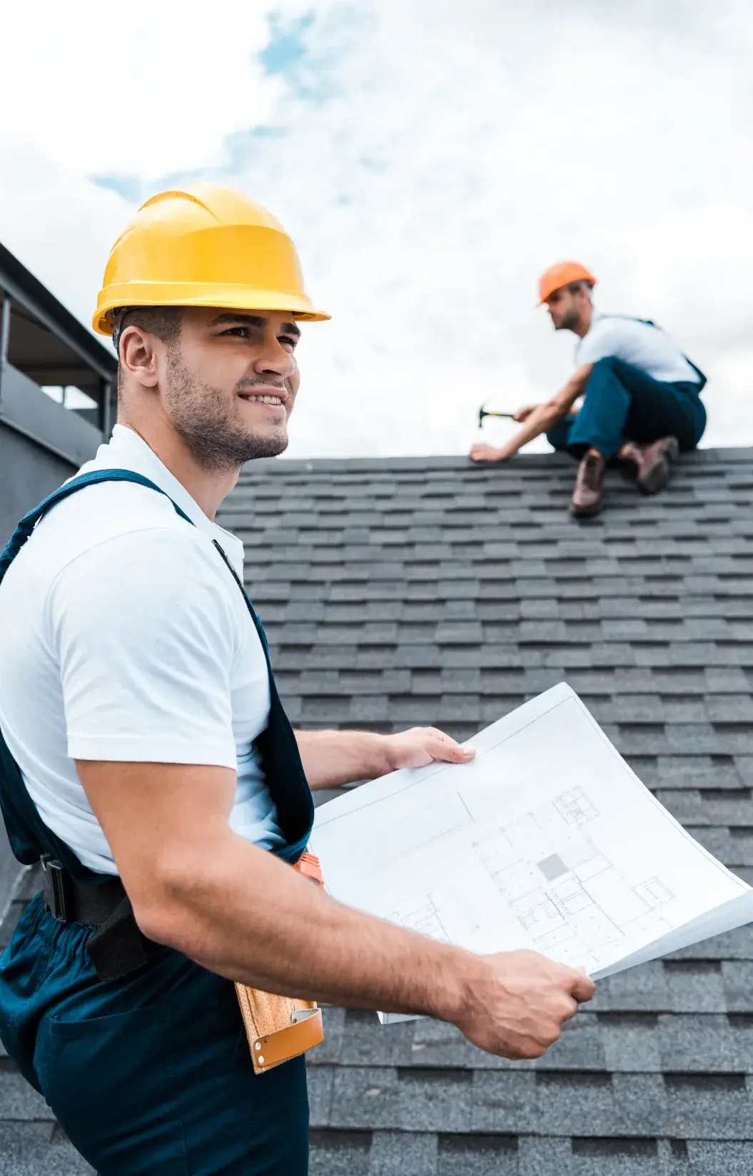 Roofing contractor holding blueprints while overseeing a roof installation.