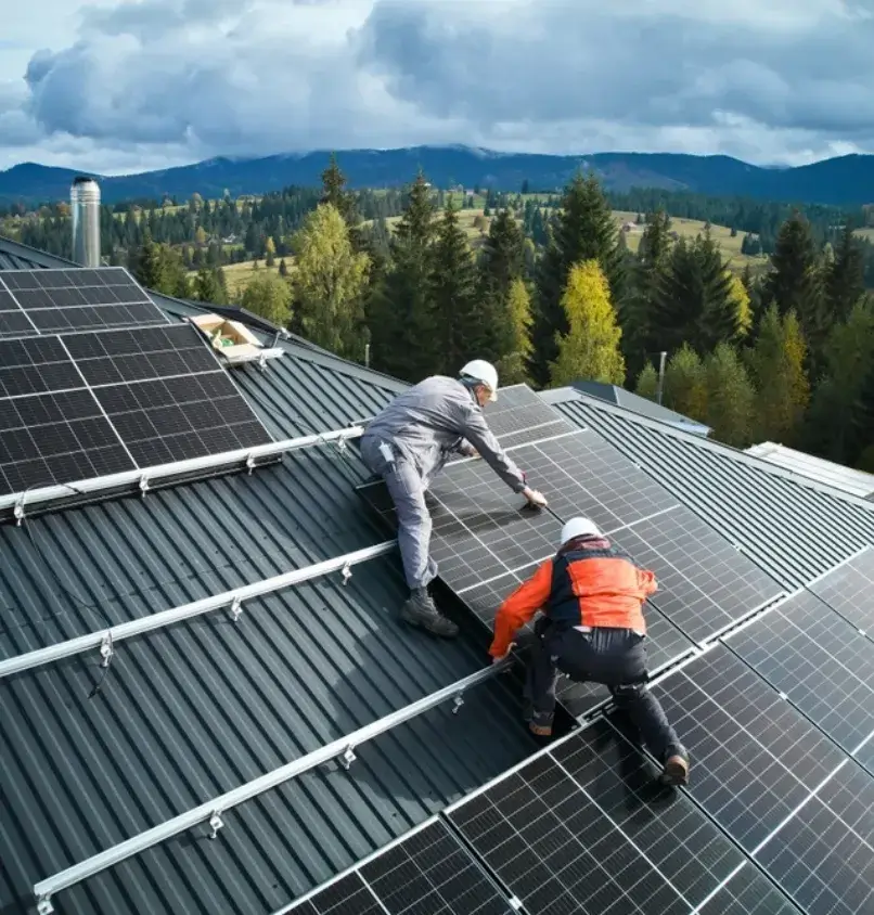 Workers installing solar panels on a metal roof in a scenic mountainous area.