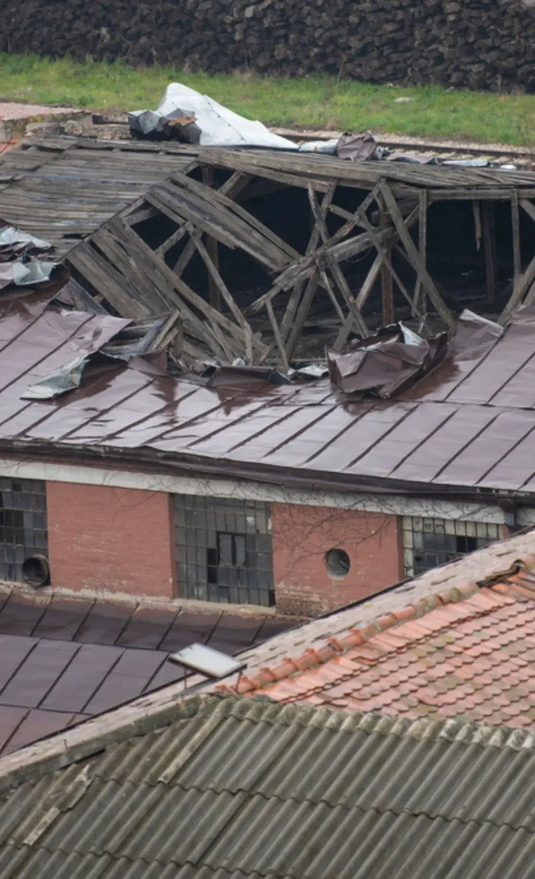 Collapsed wooden roof of an old industrial building with rusted metal sheets and broken windows.