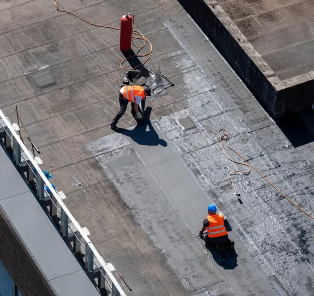 Workers applying waterproofing material on a flat commercial roof.