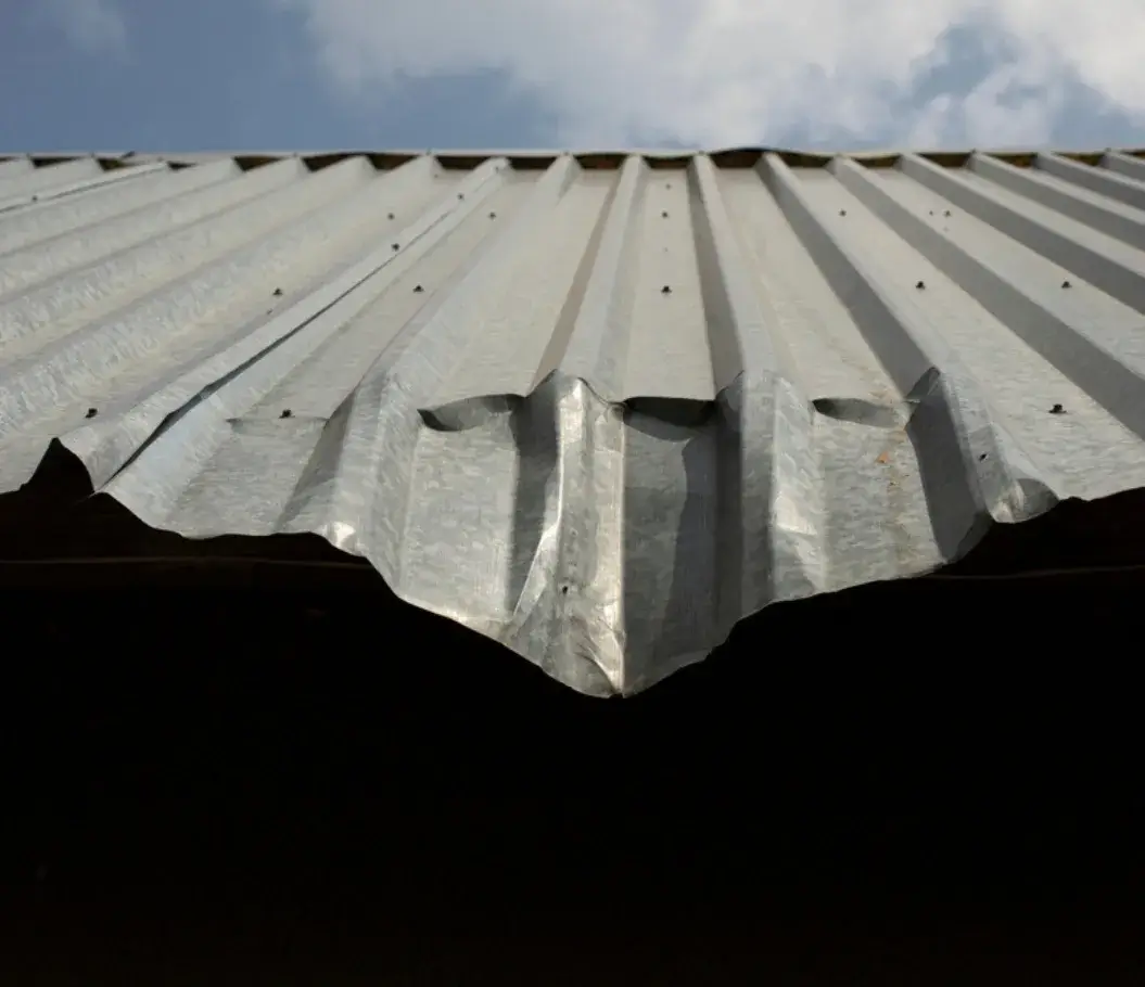 Close-up of a damaged corrugated metal roof with a bent and dented edge.