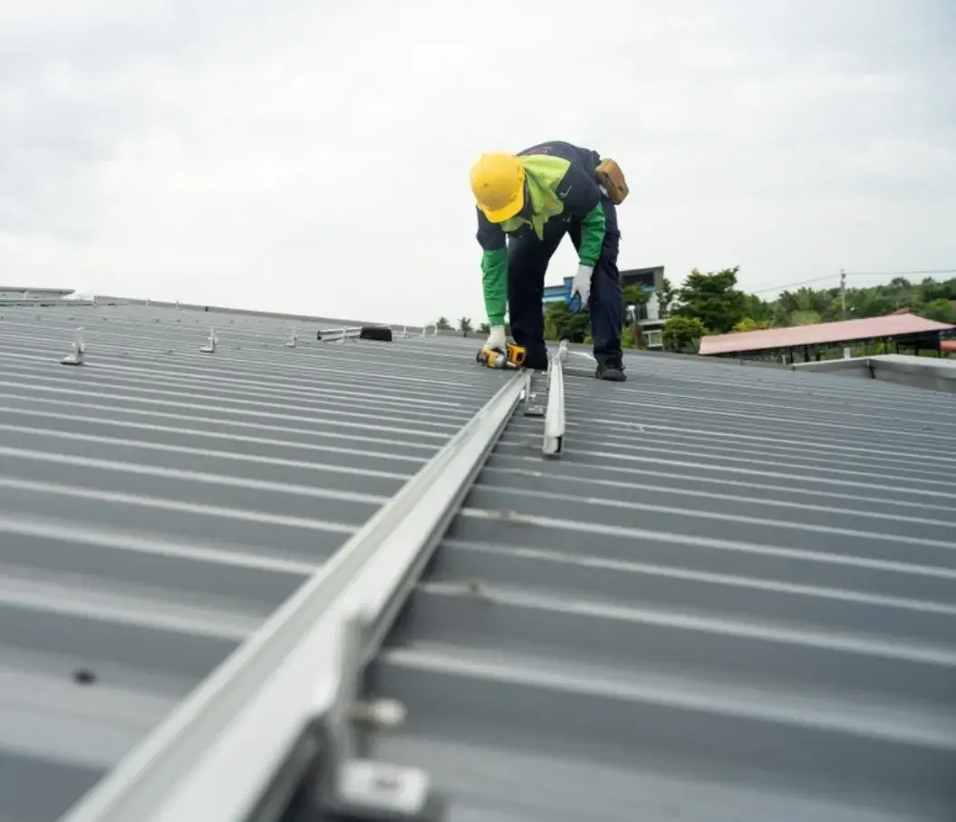 Roofer installing a metal rail on a corrugated metal roof using a power drill.