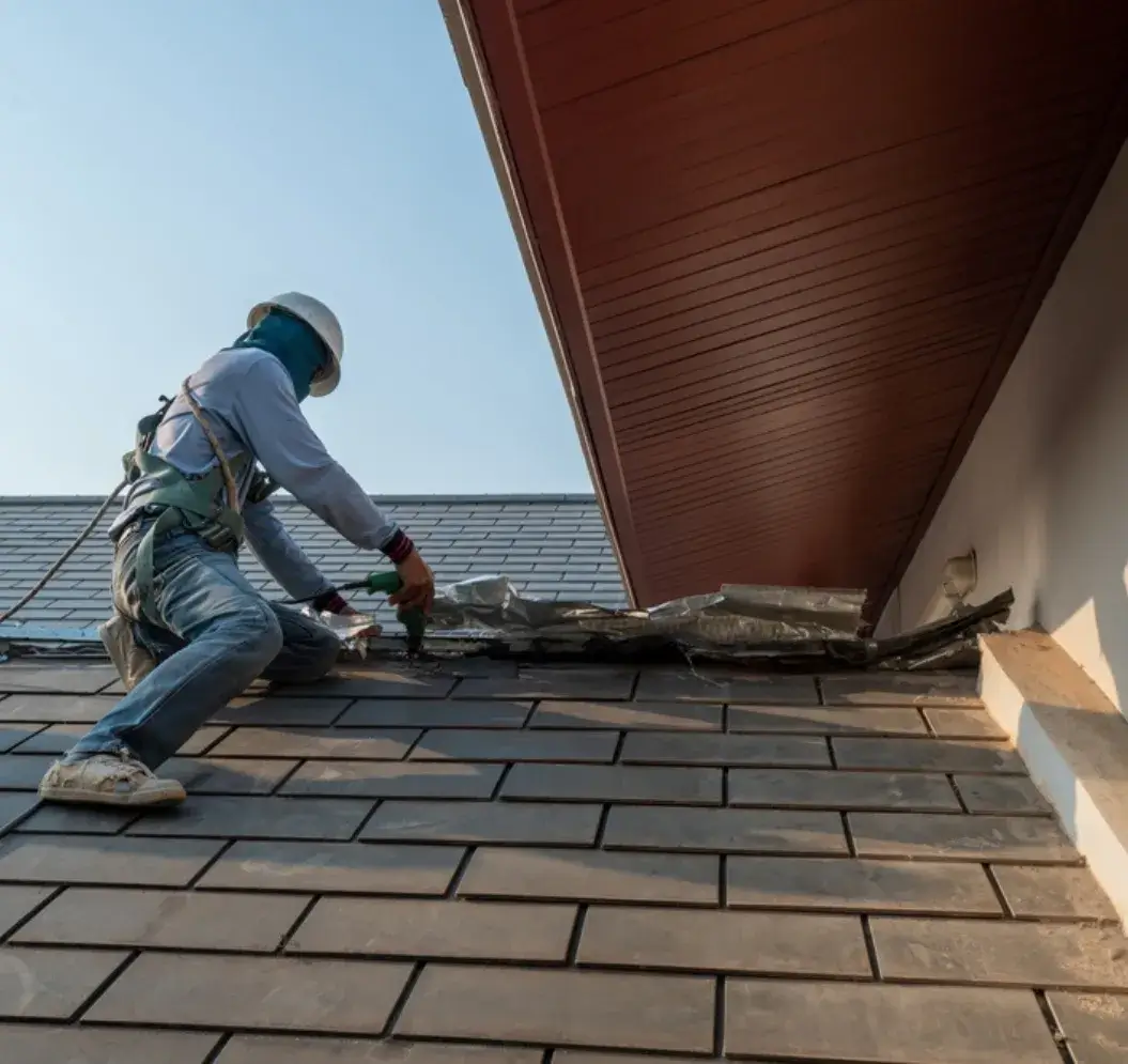 Roofer repairing a tiled roof with a power drill while wearing safety gear.