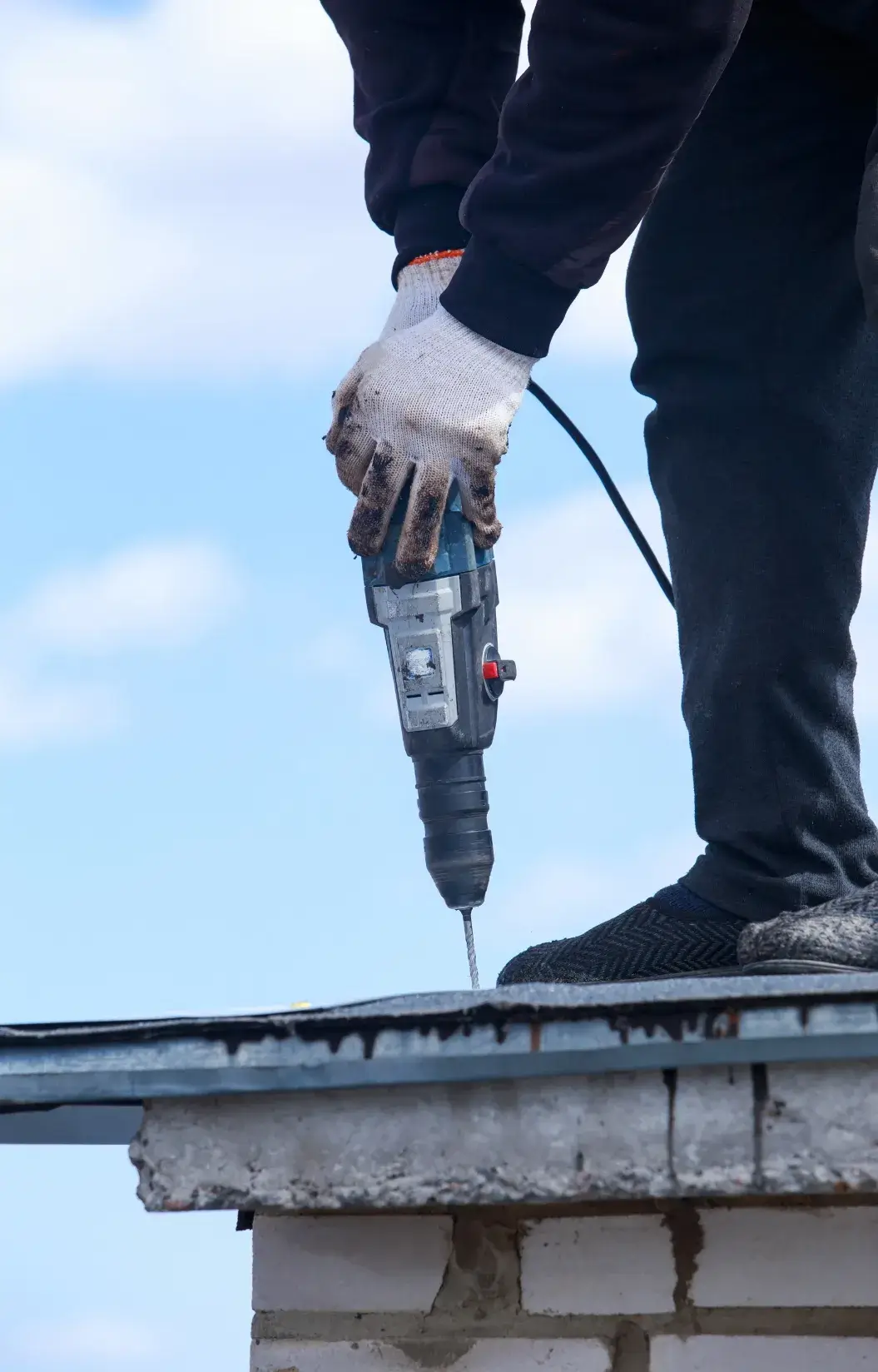 Worker using a power drill on a metal roof edge.