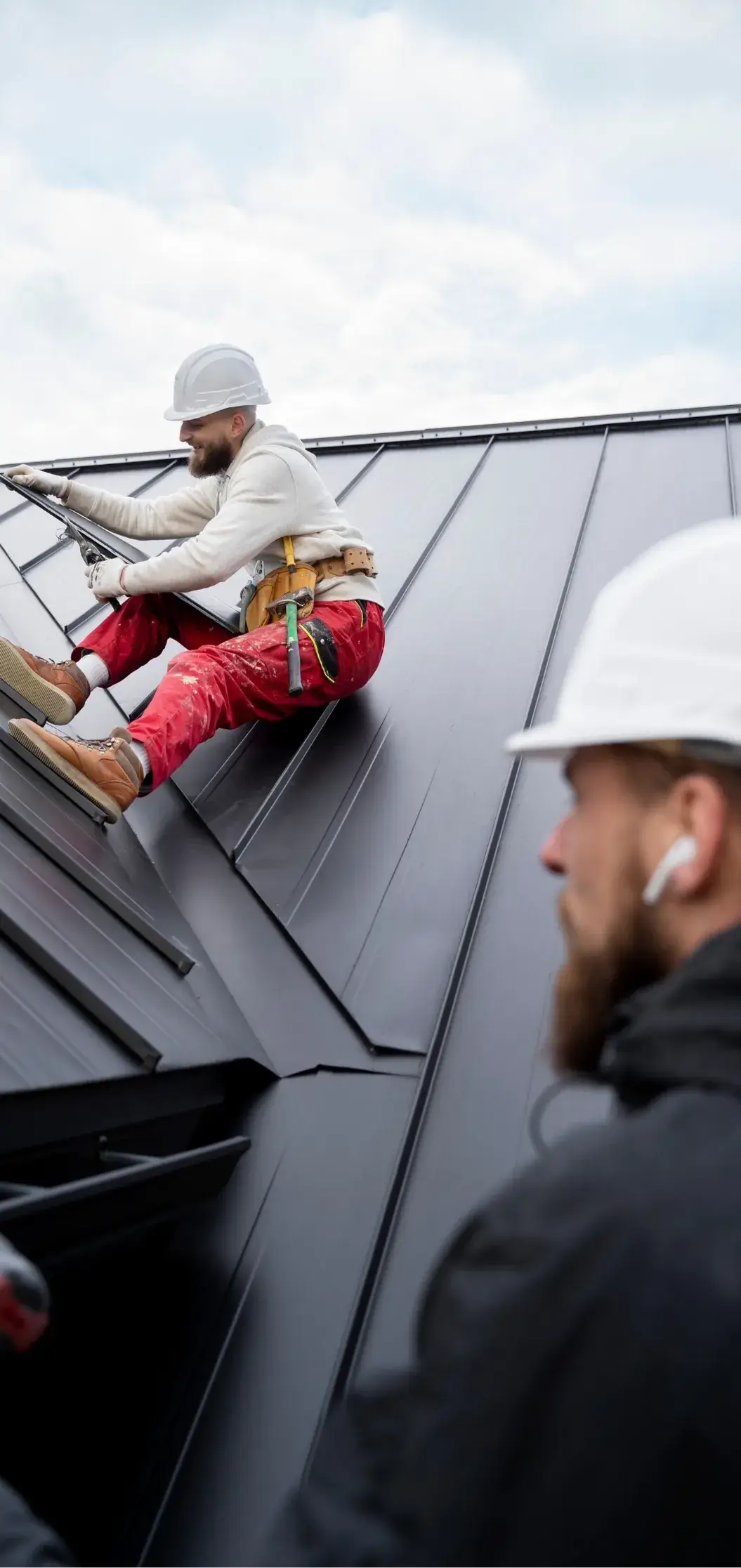 Professional roofers installing a black metal roof while using safety harnesses.